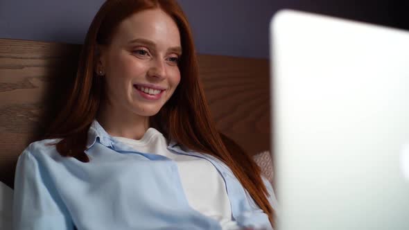 Close-up of Relaxed Redhead Young Woman Looking on Laptop Screen While Lying on Bed