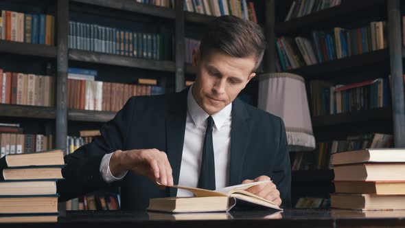 Young Man in Classical Suit Sitting in Library Searching for Information in Books