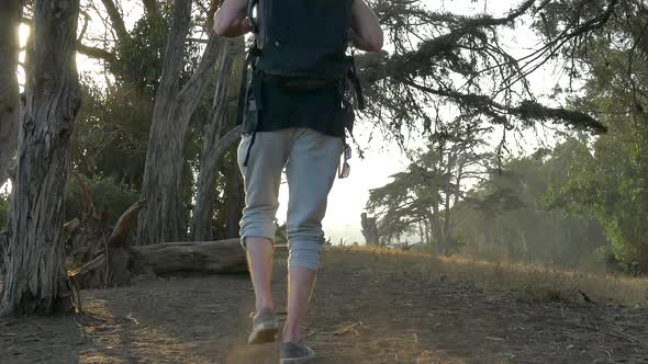 Young man traveler wearing a large black backpack walking in slow motion along the ocean bluffs duri