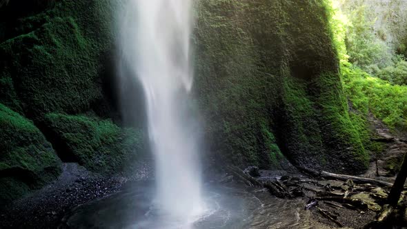 Handheld of hidden Mili Mili misty waterfall streaming into natural pond surrounded by dense green v