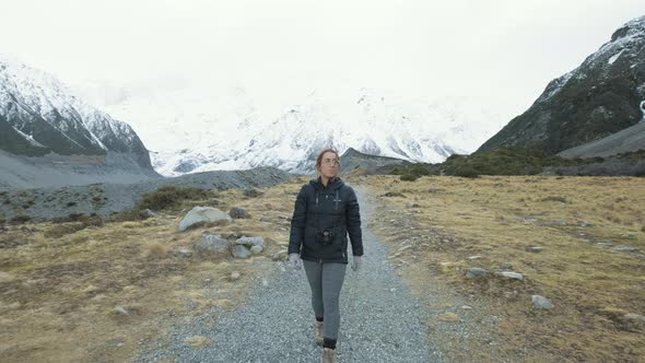 A front on following shot of a woman walking between snow capped mountains on a cold winters morning