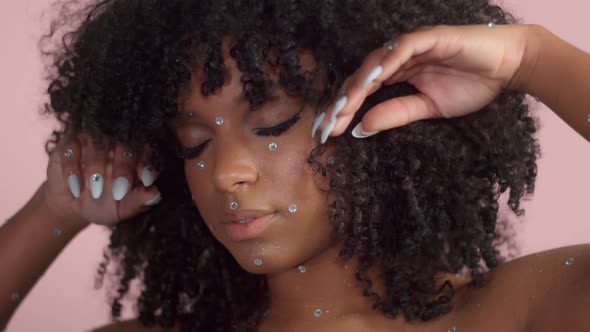 Mixed Race Black Woman with Curly Hair Covered By Crystal Makeup on Pink Background in Studio