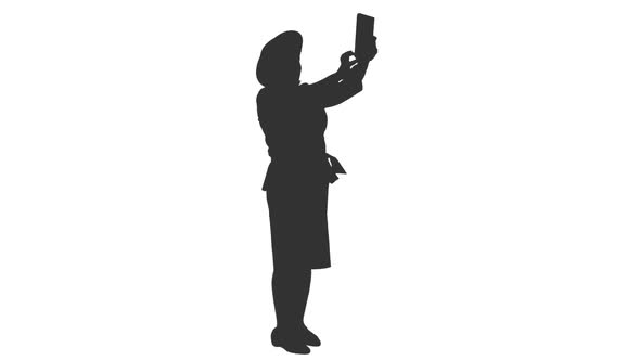 Silhouette of Elegant Woman in Hat Taking Selfie with Tablet alt