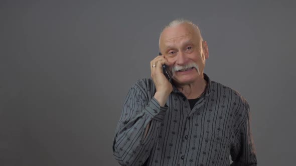 Retired Man in Dark Shirt Holds Black Smartphone and Talks