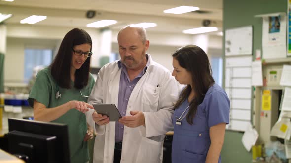 Nurses and doctor collaborate on a tablet computer in hospital.