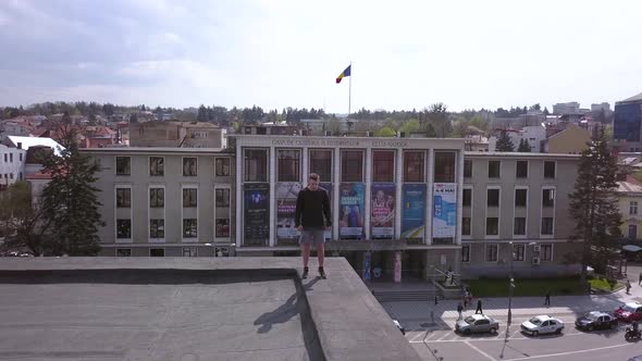 Aerial Drone Shot Pulling Back to Reveal a Young Adult Male Parkour Runner Standing on the Edge of a