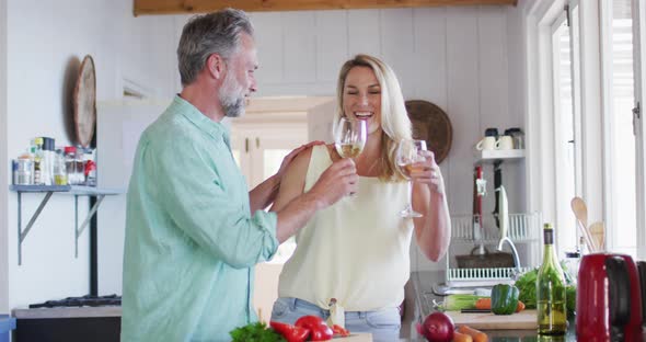 Happy caucasian mature couple cooking together and drinking wine in the kitchen