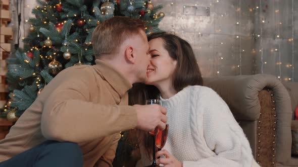 Young Couple Kissing Near the Christmas Tree While Drinking Champagne