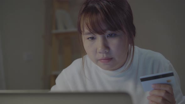 Asian woman using laptop buying online shopping by credit card sitting on desk in the night.