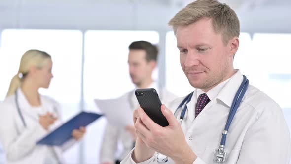 Portrait of Focused Male Doctor Using Smartphone in Office