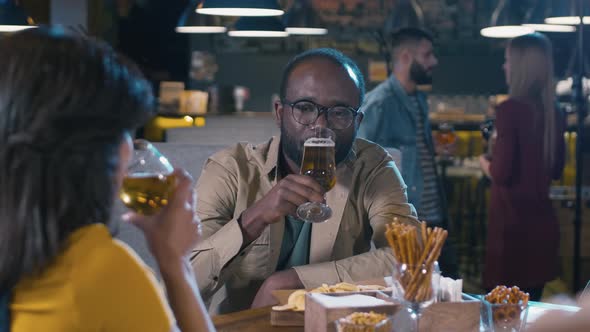 Happy multi-ethnic couple sitting in bar and clinking glasses