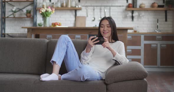 Asian Young Girl Lying in Sofa Having Video Chat on Smartphone Casual Conversation at Home