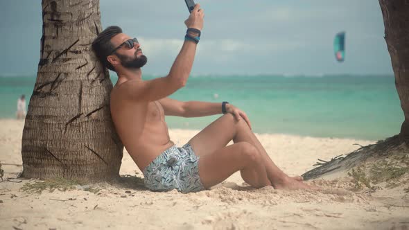 Man Sitting And Talking On Smartphone On Vacation Lounge Sea. Man Relaxing On Tropical Beach.
