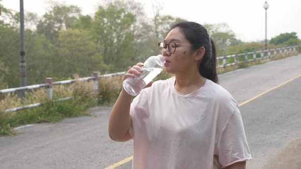 Fat woman with acne and glasses drinking water at outdoors