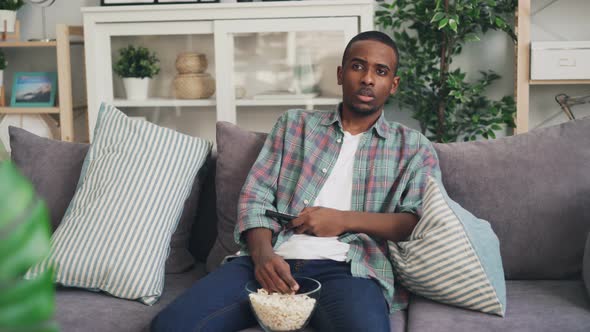 Emotional African American Man Is Watching Thriller on TV at Home and Eating Popcorn Sitting on