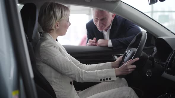 Young Blond Caucasian Woman Taking Car Keys From Dealer and Starting Engine. Elegant Rich