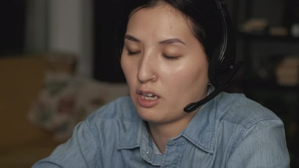 Close-Up of a Young Asian Woman Wearing Headphones with a Microphone for Work