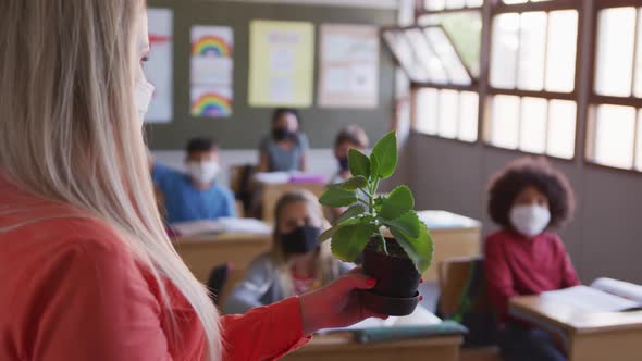 Female teacher showing a plant pot to group of kids in class at school