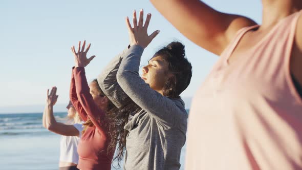 Group of diverse female friends practicing yoga at the beach