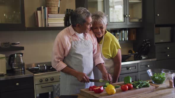 Happy senior mixed race couple wearing aprons preparing food in kitchen