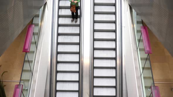 Woman using cell phone while riding down escalator