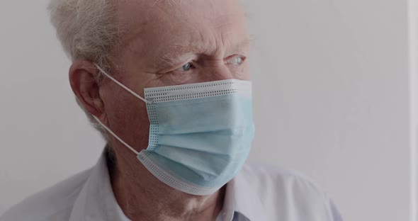 Lonely Grandfather in Mask Looking Thoughtfully at Light Window on Background