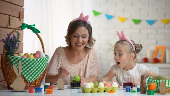 Little Girl Excitedly Watching Mother Dipping Egg in Green Food Coloring, Easter