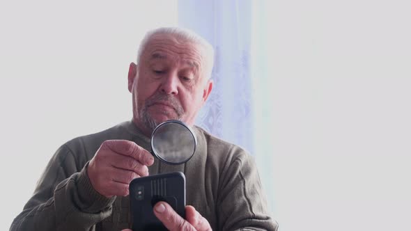 Senior Grayhaired Grandfather Reads Through a Magnifying Glass
