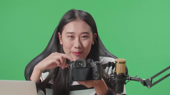 Asian Woman With Computer Reviewing Camera While Sitting In Front Of Green Screen Background