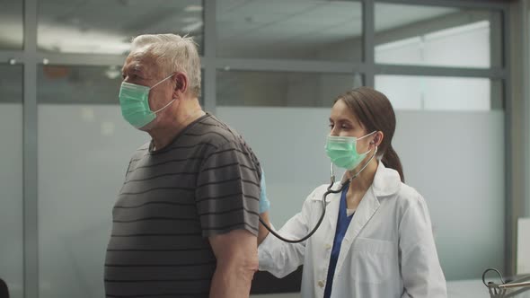 Therapist Girl Performs Auscultation of the Lungs From the Back of an Old Patient with Pneumonia