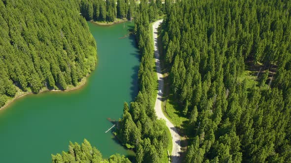 Aerial view of car driving through the fores and the lake on the side. Beautiful mountain road