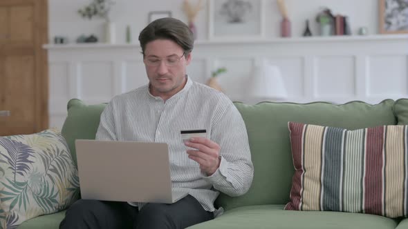 Man making Online Payment on Laptop on Sofa