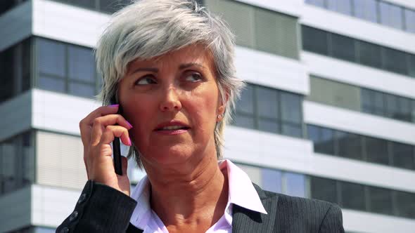 Business Middle Age Woman Calls with the Smartphone - Company Building in the Background - Closeup