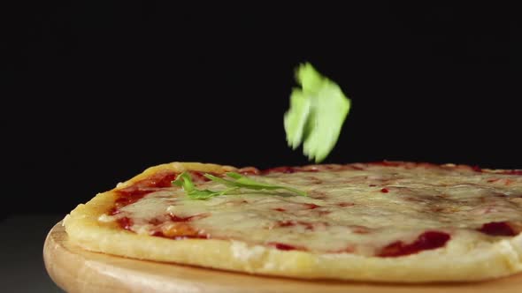 Basil Slices Fall On A Rotating Pizza On A Black Background