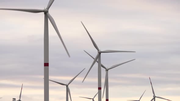 Motion the Blades of a Large Wind Turbine in a Field Against a Background of Orange Sunset on the