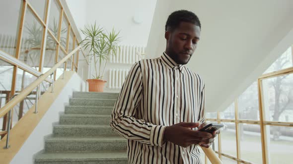 Afro-American Man Standing on Staircase and Using Smartphone