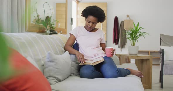 Happy african american woman sitting on sofa, reading book