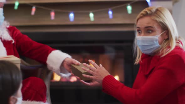 Santa Claus wearing face mask giving the gift box to mother and daughter