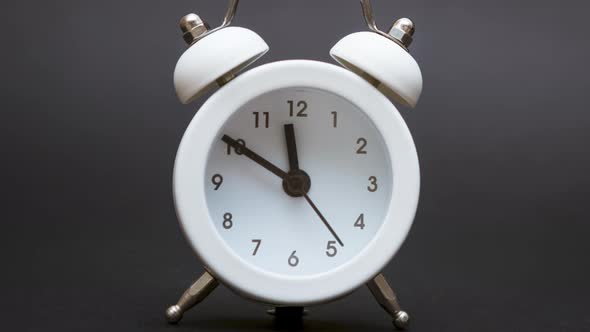 A White Alarm Clock on a Black Background Shows Ten Minutes to Twelve