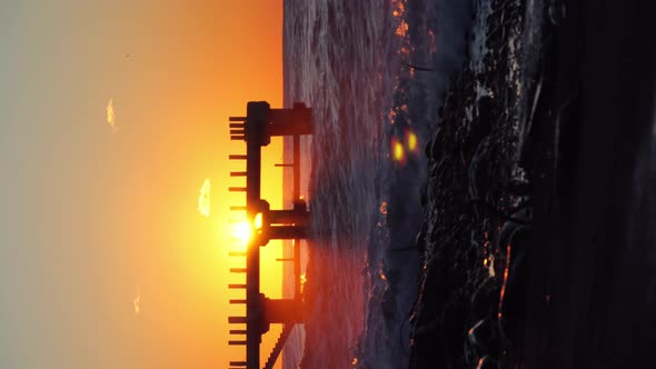 hot storm waves hit the pier at sunset. Beautiful orange sky, crashing waves.