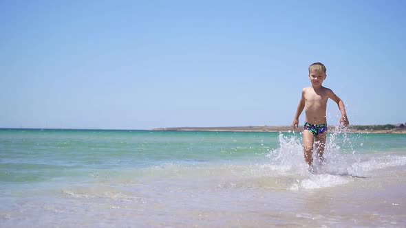 Happy Child Runs Along a Sandy Beach on the Background of a Beautiful Azure Sea.