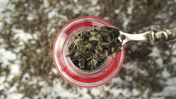 Green Tea. Dried Rolled Leaves Falling Into a Glass Teapot Close-up