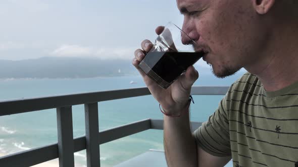 Caucasian Man Drinking Coffee at Balcony with Amazing View of Sea and Mountain