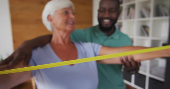 Video of happy caucasian senior woman exercising with african american male physiotherapist