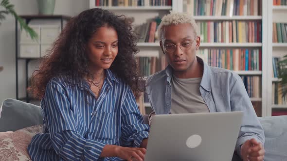 Mixed Ethnic Couple Sit Relax on Couch in Living Room Choose New Goods on Laptop