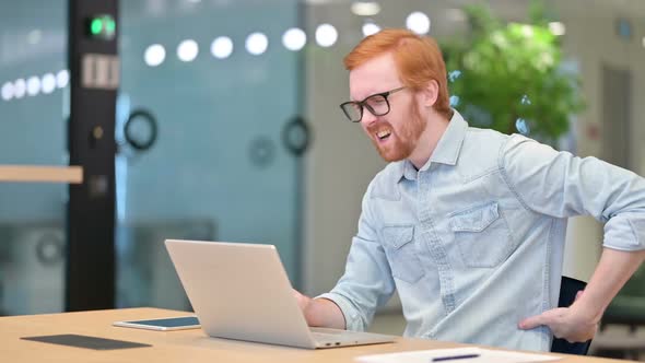 Young Redhead Man with Laptop Having Back Pain in Office