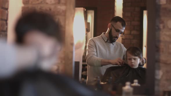Hairdresser cutting hair of child in Barbershop