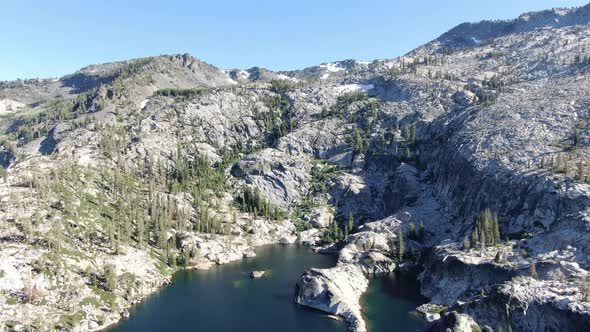 A slow high resolution drone shot flies backward to reveal a deep clear alpine lake at the bottom of