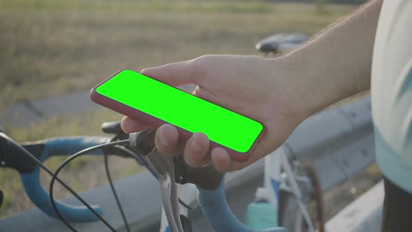 A Man Holds a Modern Smartphone with a Green Chromakey Screen While Standing Next To a Bicycle