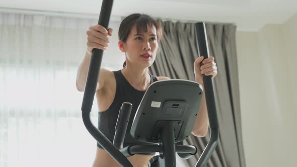 Asian young active sport woman feeling tired while working out exercise on cycling machine at home.